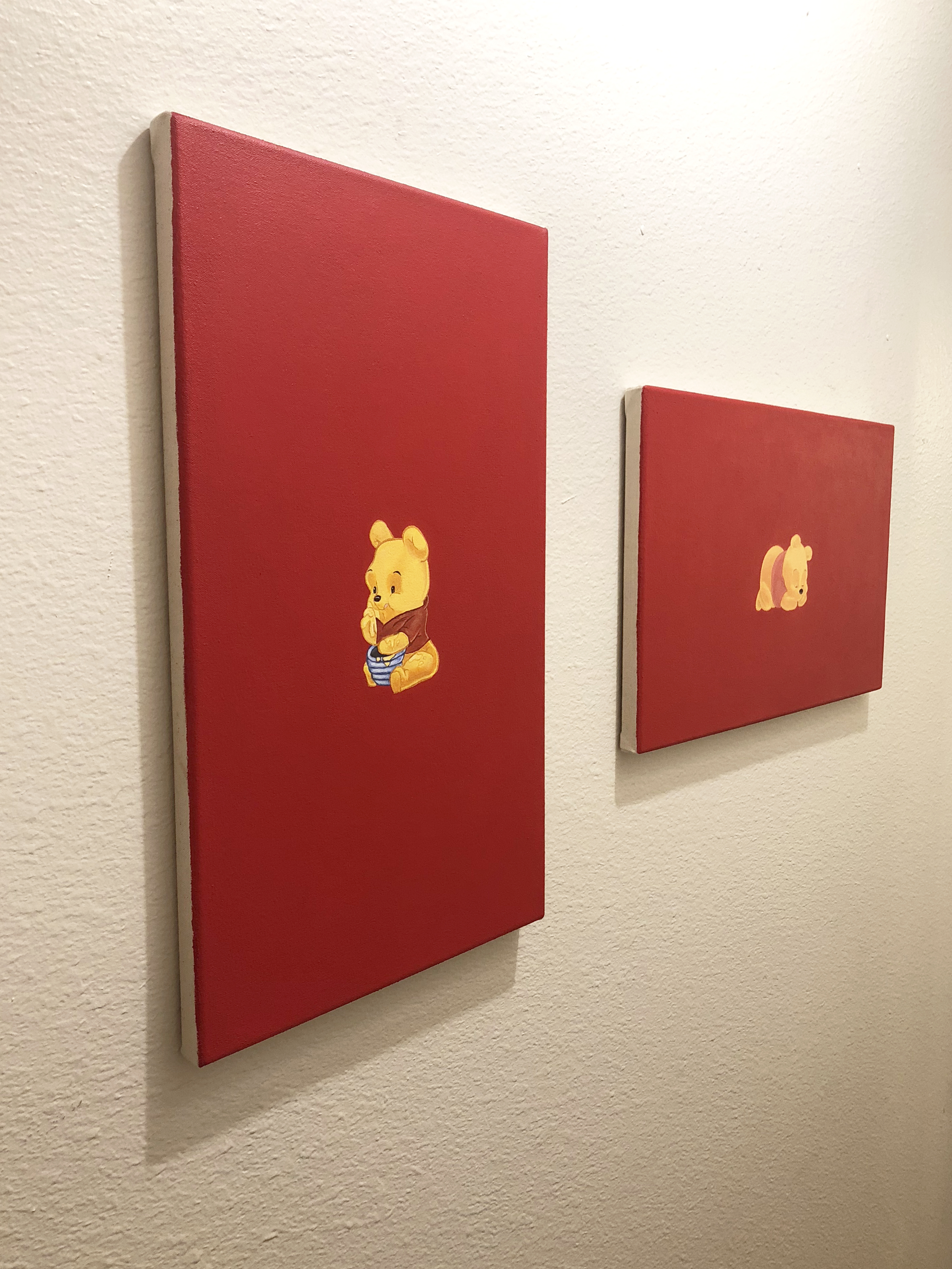 Two paitings of winnie the pooh on a red background hung on a white wall